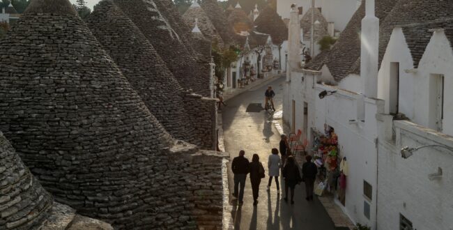 High Angle View Of People Walking On Street Amidst Trullo Houses With Conical Roofs In Alberobello